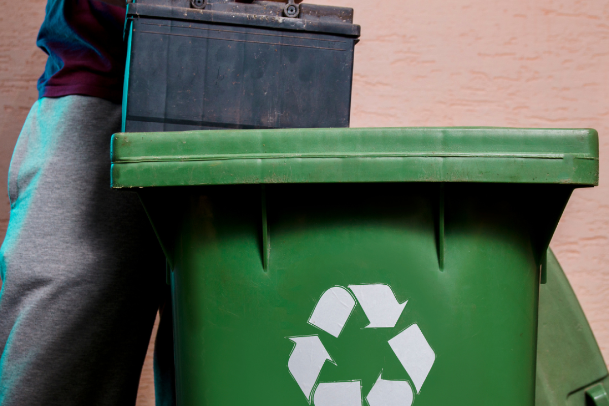 Person wirft Akku in Recycling-Mülltonne.